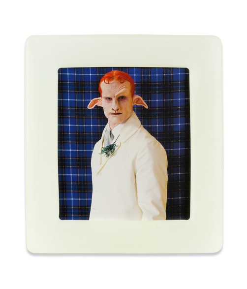 An image of a red-haired person with animal-like ears and nose wearing a white suit in front of a blue plaid backdrop, beside a recreated image of a person wearing a backwards baseball cap with white floppy ears in front of a red plaid backdrop.