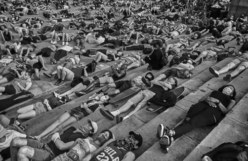 A black and white photo of protesters lying down on concrete stairs.