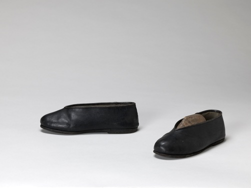 A black, low-heeled pair of leather shoes with low-cut tops and upturned toes.