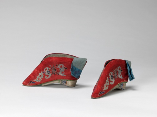 Red satin shoes with intricately embroidered bats, Chinese symbols, and serpentine shapes in light blue-shaded thread.