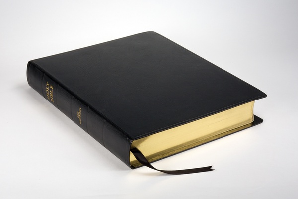 A black leather-bound book with gilded page edges and "HOLY BIBLE" and "OLD TESTAMENT" gilded on its spine.